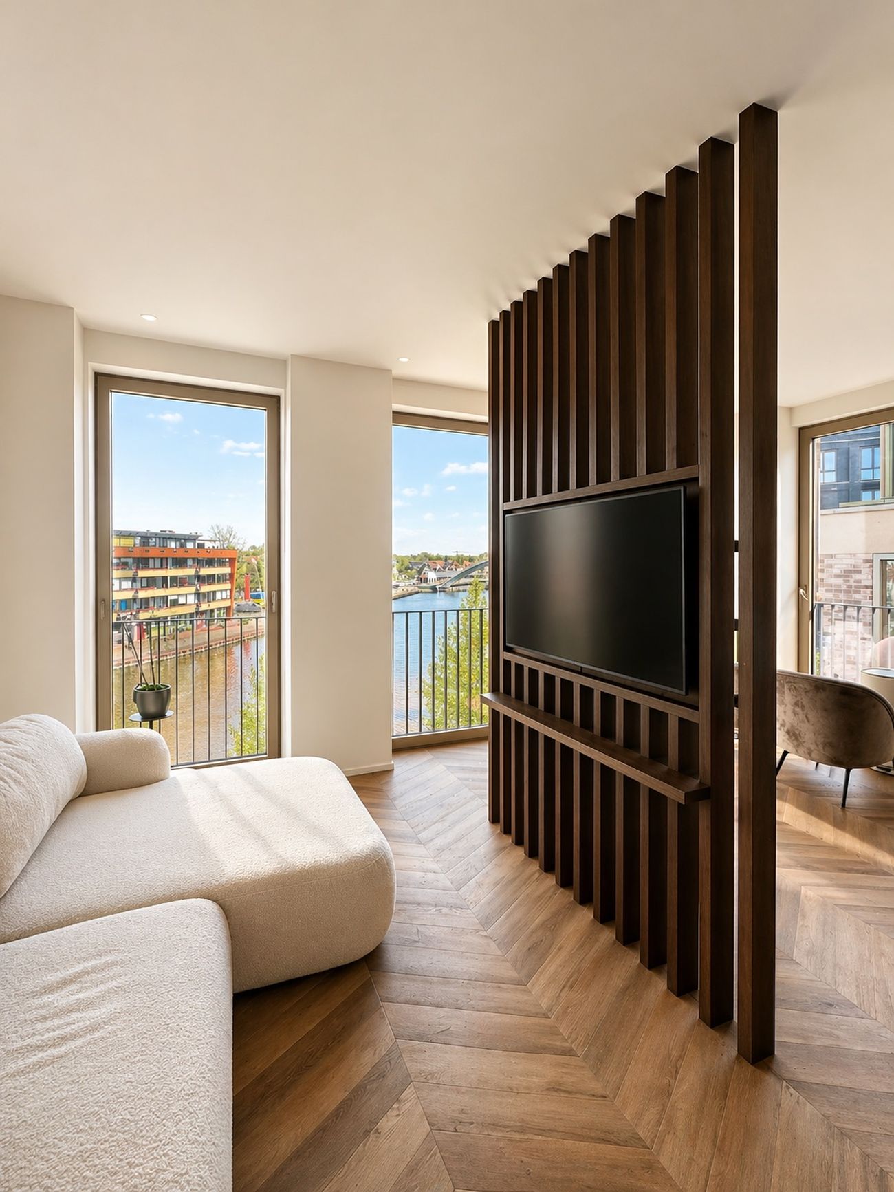 Lichte woonkamer met visgraatvloer, houten lamellenwand en uitzicht op het water